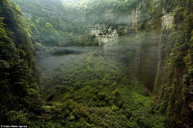 Вид из маленького окна в стене огромного карстового массива Niubizi Tian Keng в пещерной системе Er Wang Dong, здесь образуются облака внутри огромных внутренних пространств. Если Вы присмотритесь - сможете найти трех крошечных по размеру людей среди бурной растительности