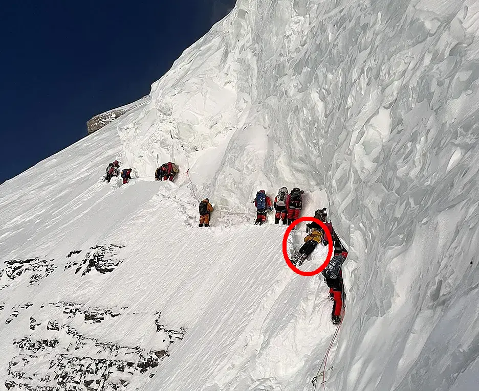 Траверс під Великим Сераком на К2. 27 липня 2023 року. Альпіністи йдуть до вершини, причеплені до мотузки, а Гасан лежить на снігу в чорних штанях і жовтій куртці (обведено колом). Фото: Lakpa Sherpa/8K Expeditions